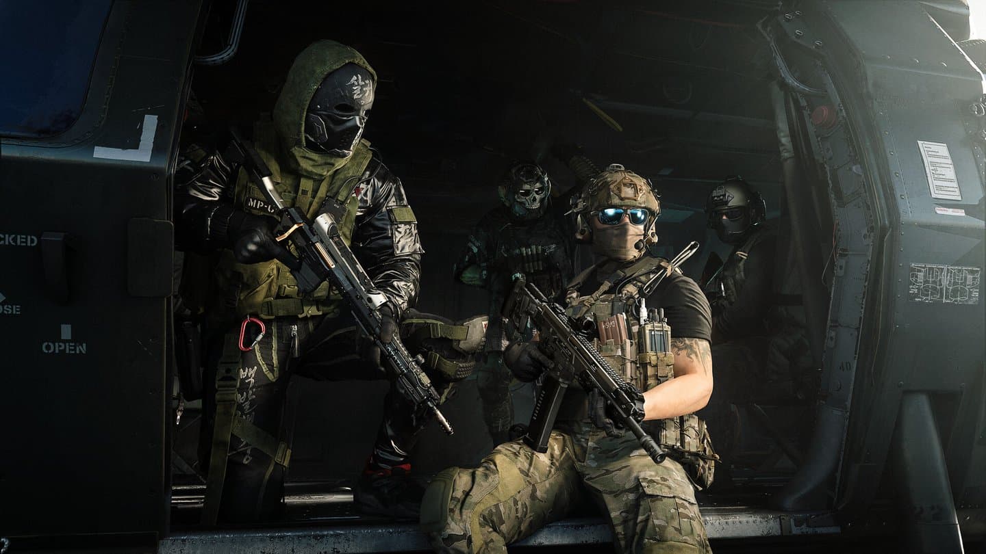 Four soldiers in the open door of a helicopter, one in a green hood and a black mask, rifles in hand.