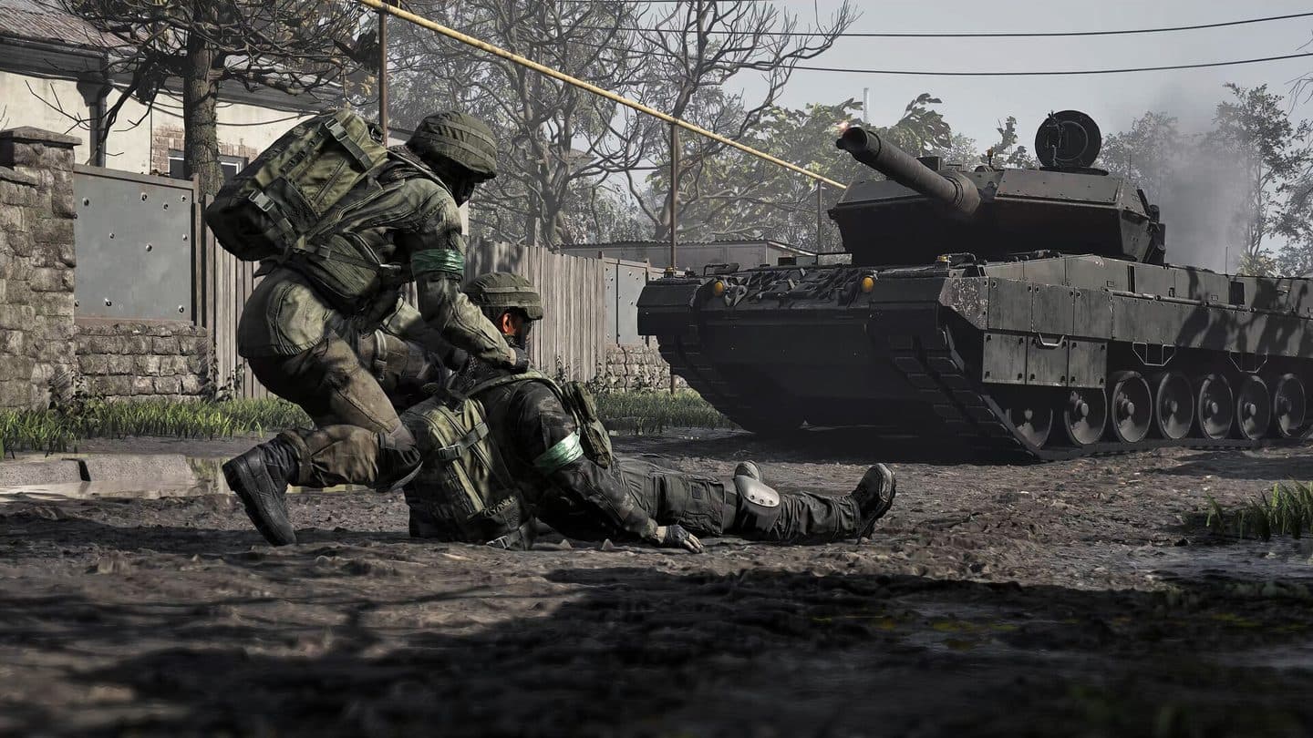 A WARDOGS soldier drags a wounded teammate out of the mud while a tank fires behind them.
